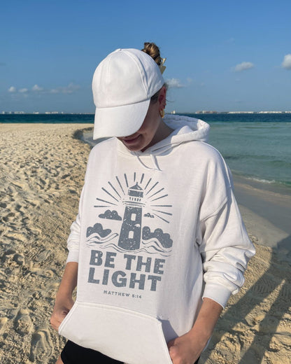 Woman wearing white Be The Light Christian hoodie on beach