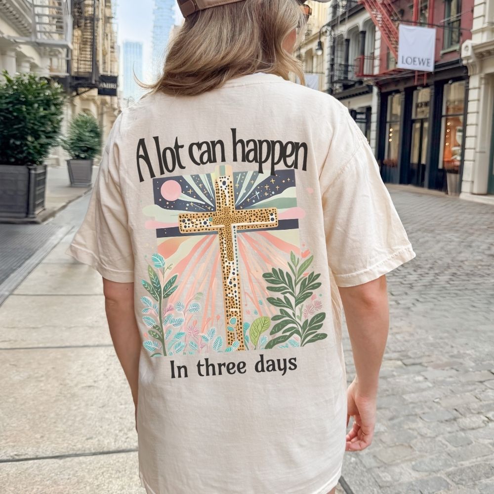 Person wearing a t-shirt with a cross design and text on the back, walking down a city street.