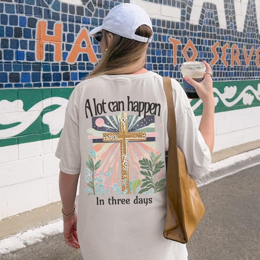 Person wearing a t-shirt with a cross design and text, standing in front of a mosaic wall.