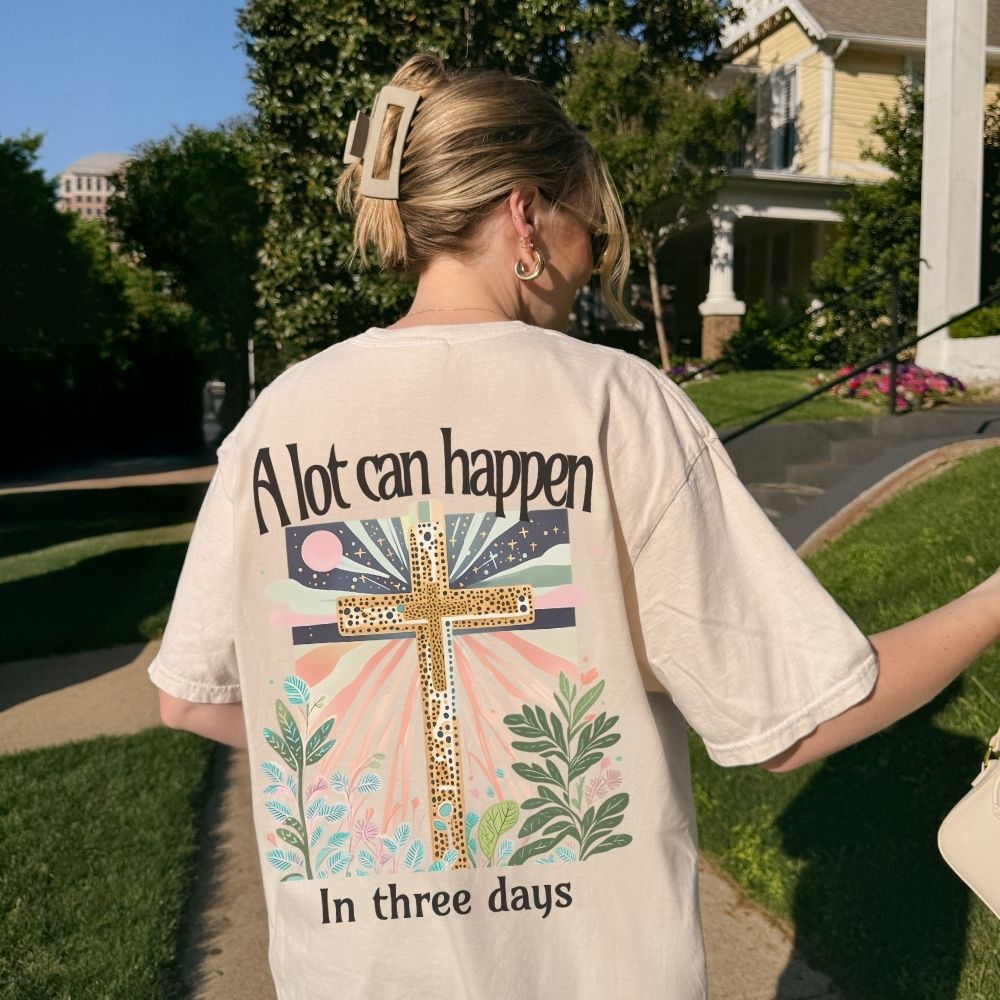 Person wearing a t-shirt with a cross design and text outdoors.