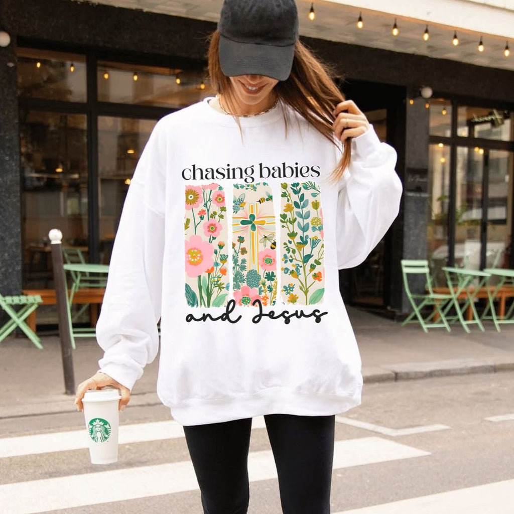 Person wearing a white hoodie with floral design and text, holding a Starbucks cup on a city street.