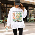 Person wearing a white hoodie with floral design and text, holding a Starbucks cup on a city street.