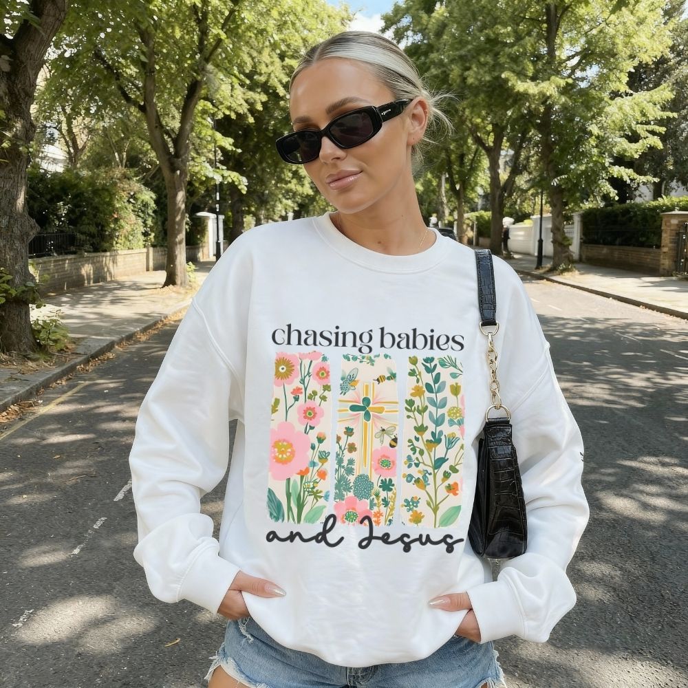 Woman wearing a white sweatshirt with a graphic design and text, standing outdoors on a sunny day.