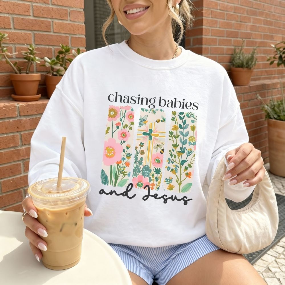 Person wearing a white sweatshirt with floral design and text, holding iced coffee.
