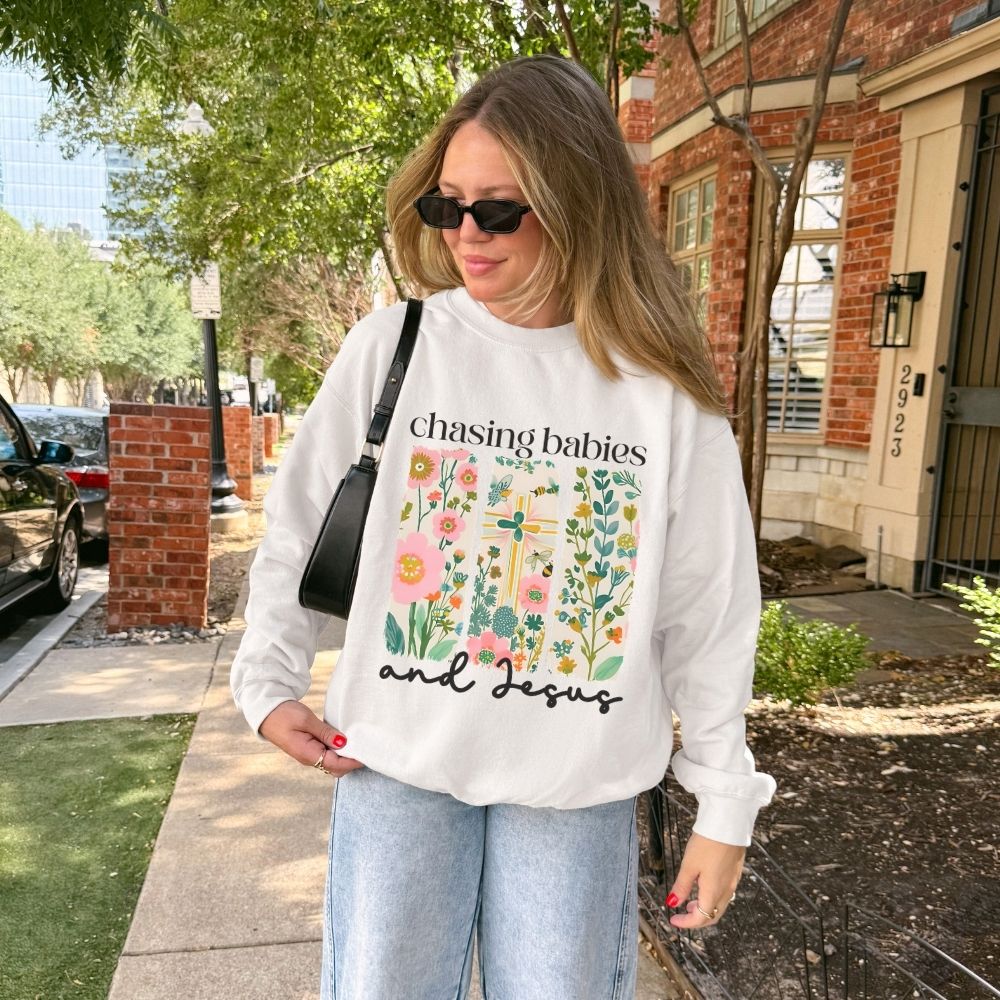 Woman wearing a white sweatshirt with floral design and text, standing on a sidewalk.