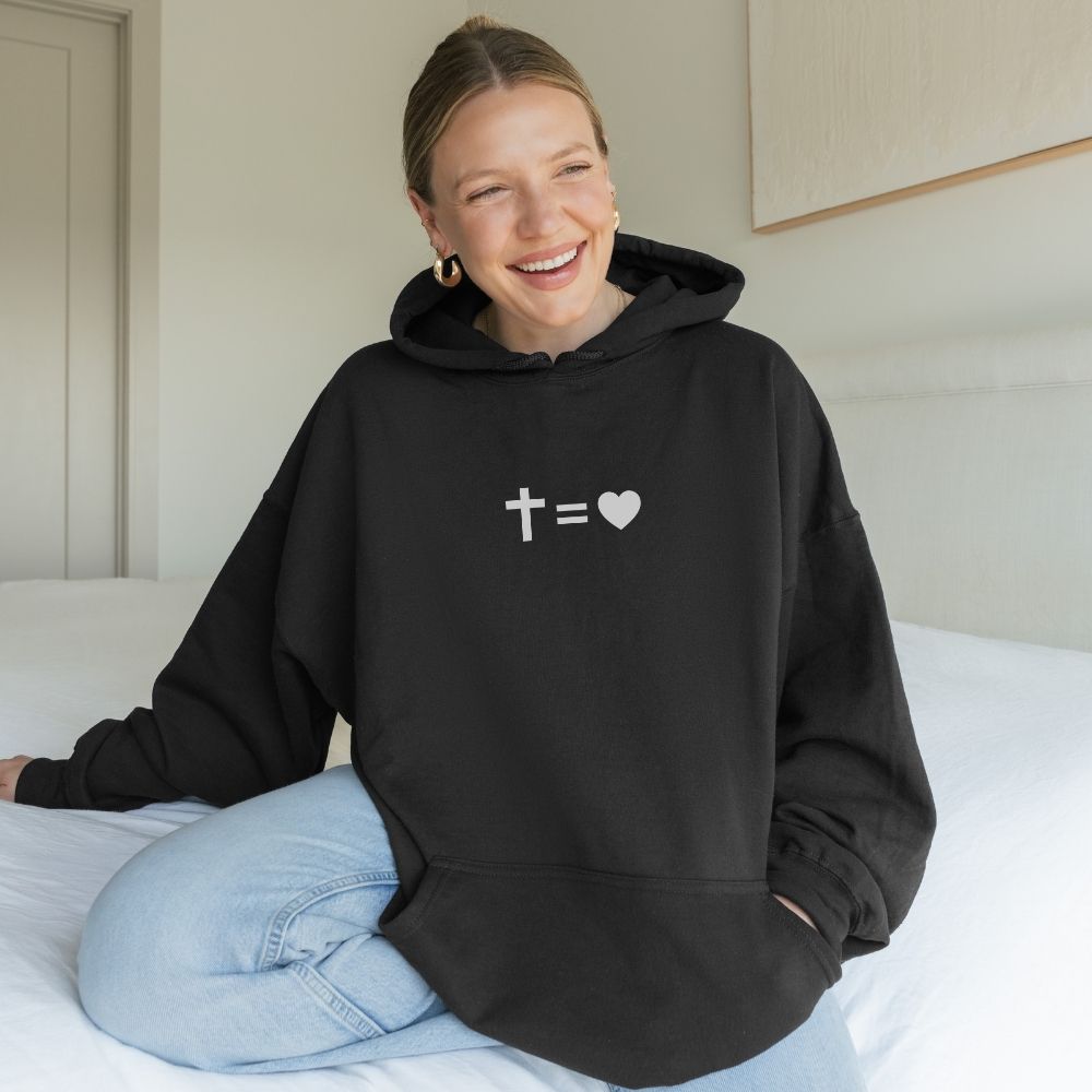 Person wearing a black hoodie with a white design sitting on a bed.