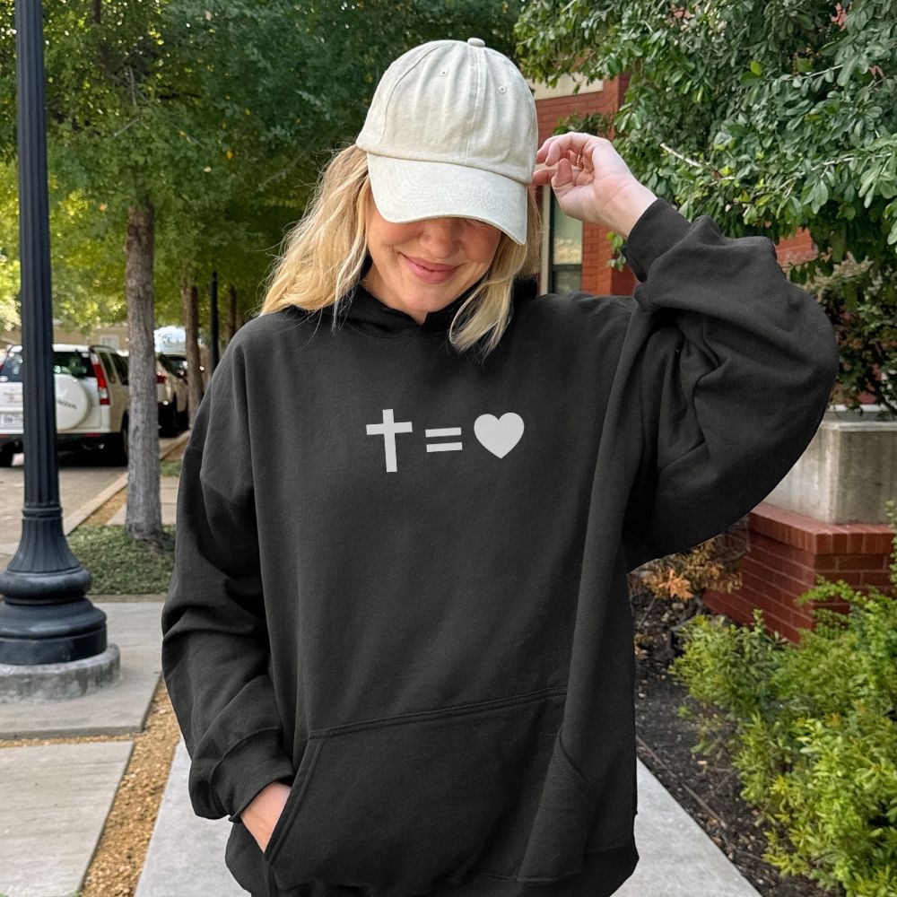 Person wearing a black hoodie with a cross and heart symbol, standing outdoors.