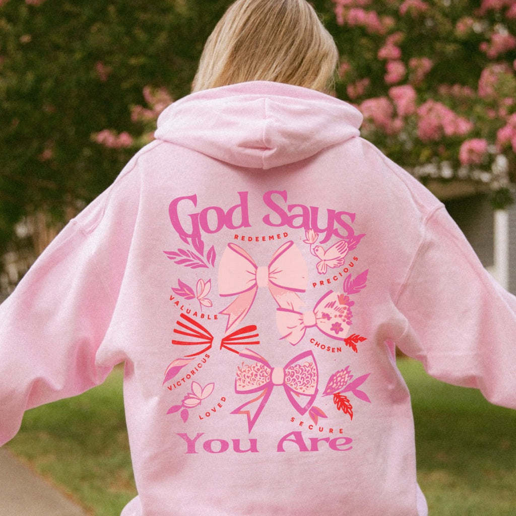 Woman wearing pink God Says You Are Christian coquette bow hoodie outdoors