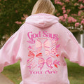 Woman wearing pink God Says You Are Christian coquette bow hoodie outdoors