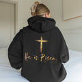 Person wearing a black hoodie with 'He is Risen' text and cross design on the back.