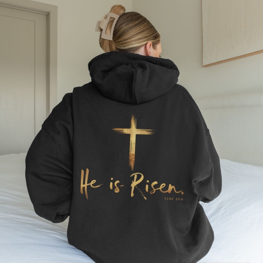 Person wearing a black hoodie with 'He is Risen' text and cross design on the back.