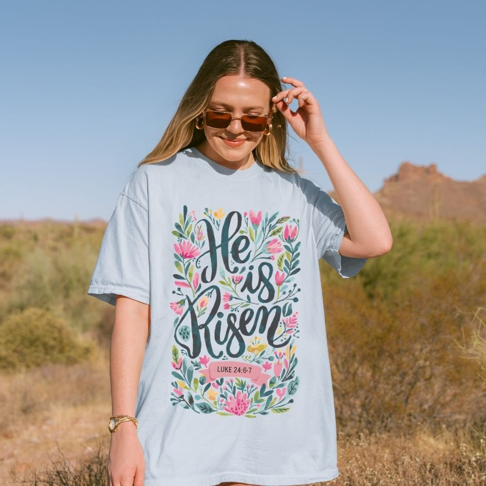 Woman wearing a t-shirt with 'He is Risen' text in a desert setting
