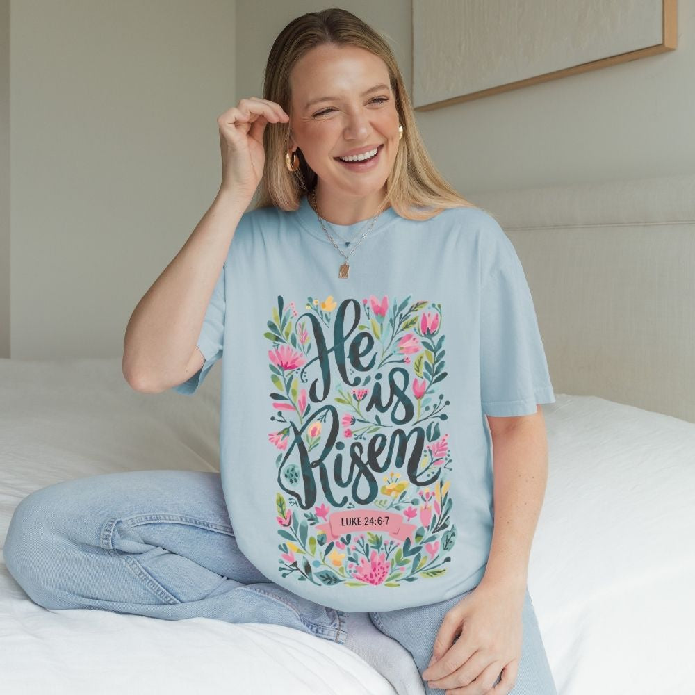 Woman wearing a light blue t-shirt with floral text design sitting on a bed.