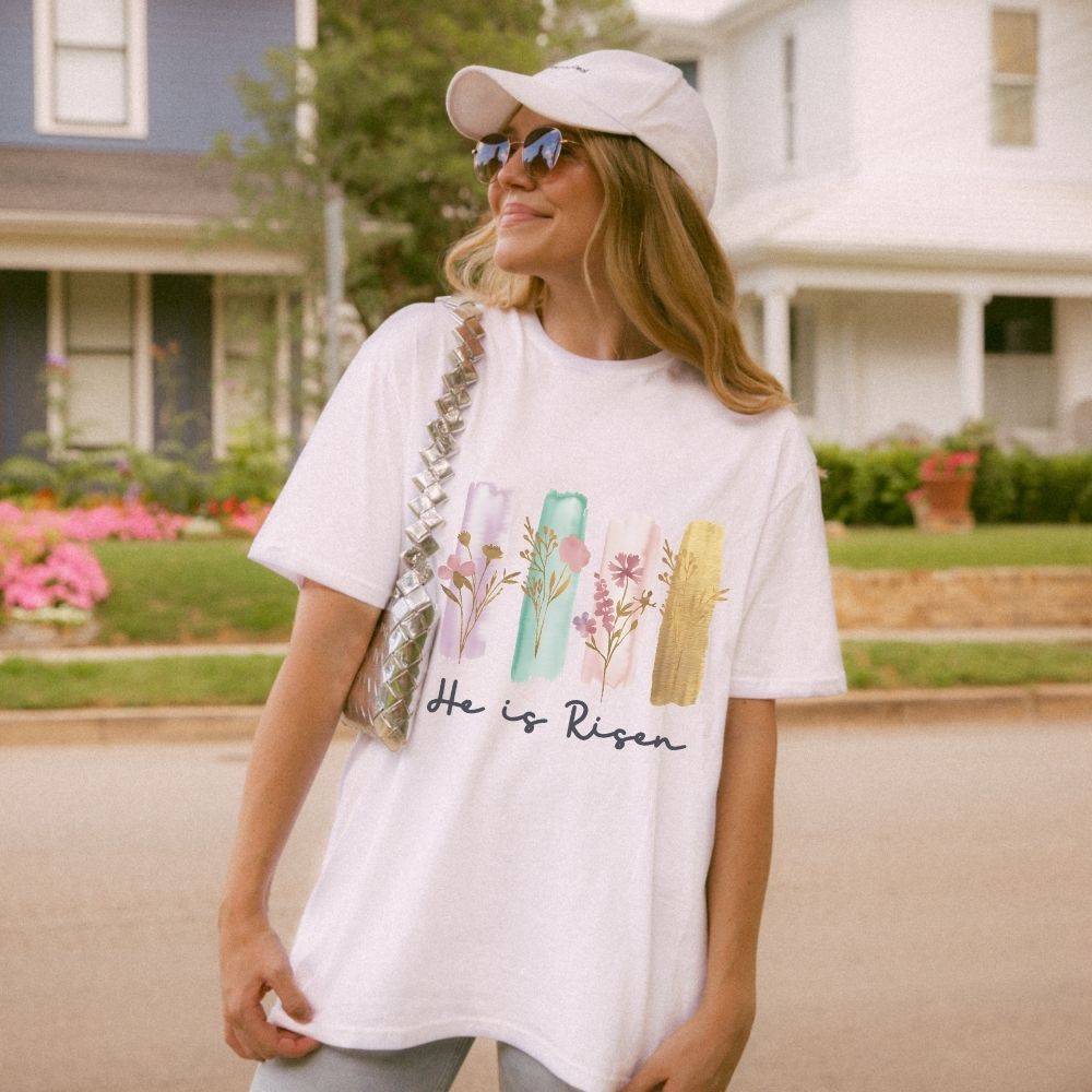 Woman wearing a white t-shirt with floral designs and text, standing outdoors.