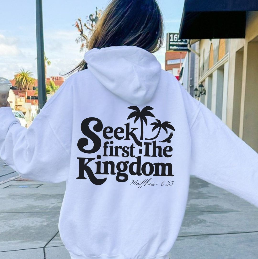 Person wearing a white hoodie with 'Seek first the Kingdom' text on the back, walking outdoors.