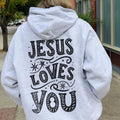 Model wearing a light grey hoodie with the text “Jesus Loves You” on the back