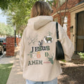 Person wearing a beige hoodie with religious text and graphics outdoors.