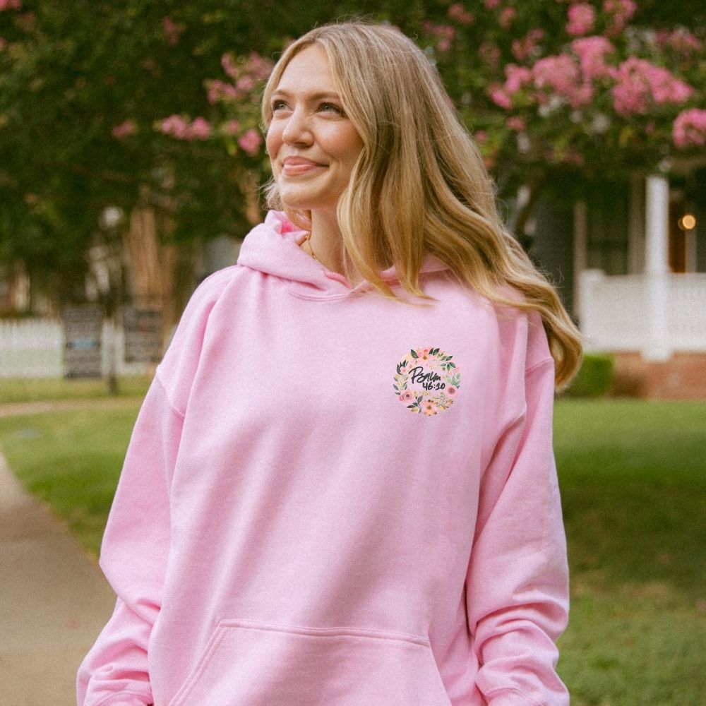 A person wearing a pink Christian hoodie with floral “Be Still and Know” design.