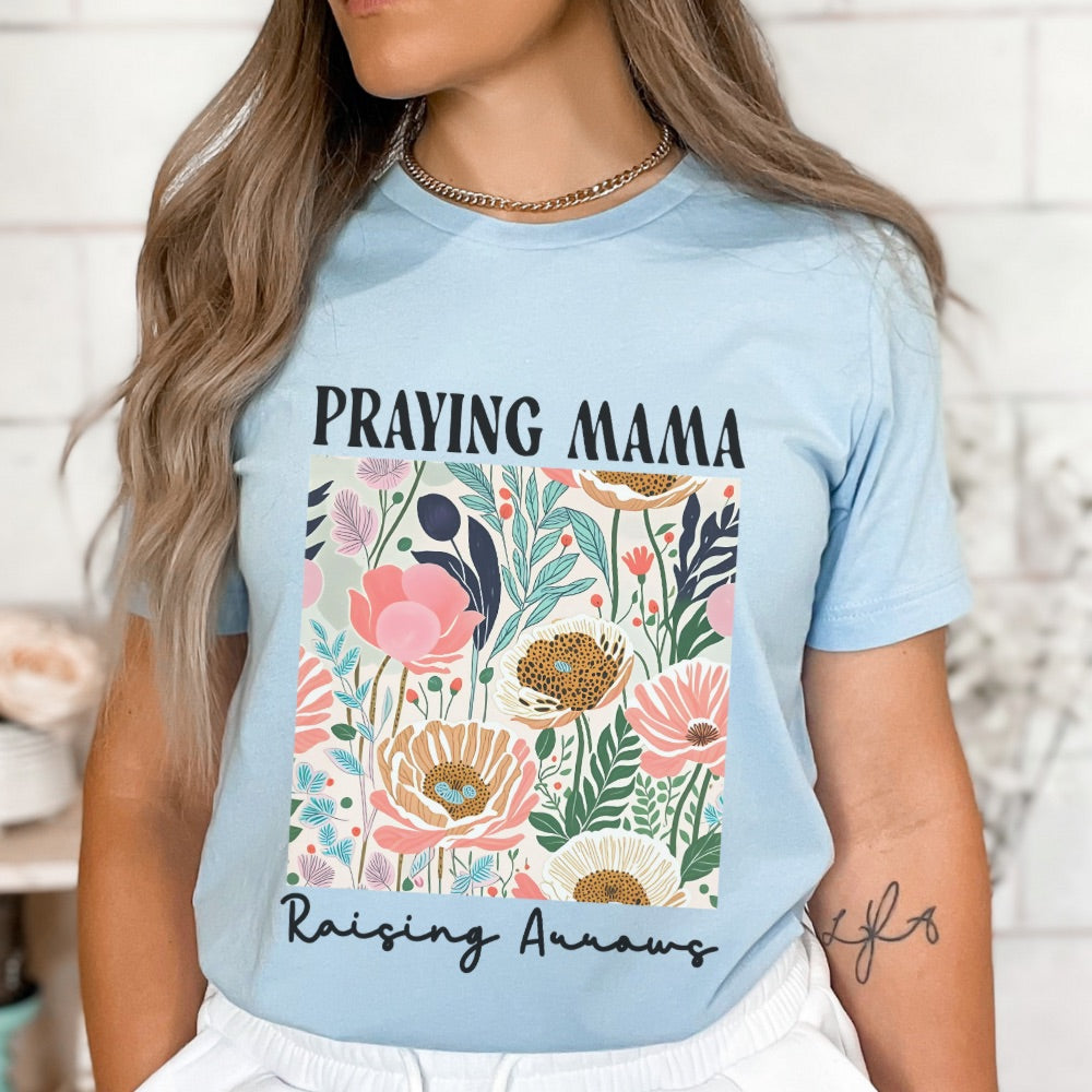 Light blue t-shirt with 'Praying Mama' and floral design, worn by a person.