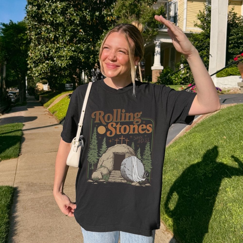 Woman wearing a white sweatshirt with a graphic design and text, standing outdoors on a sunny day.