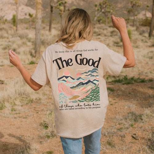 Woman wearing a cream premium tee with Romans 8:28 inspired artwork and the words “The Good” on the back
