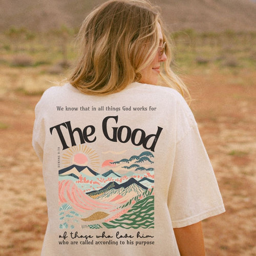 Woman wearing a cream premium tee with Romans 8:28 inspired artwork and the words “The Good” on the back