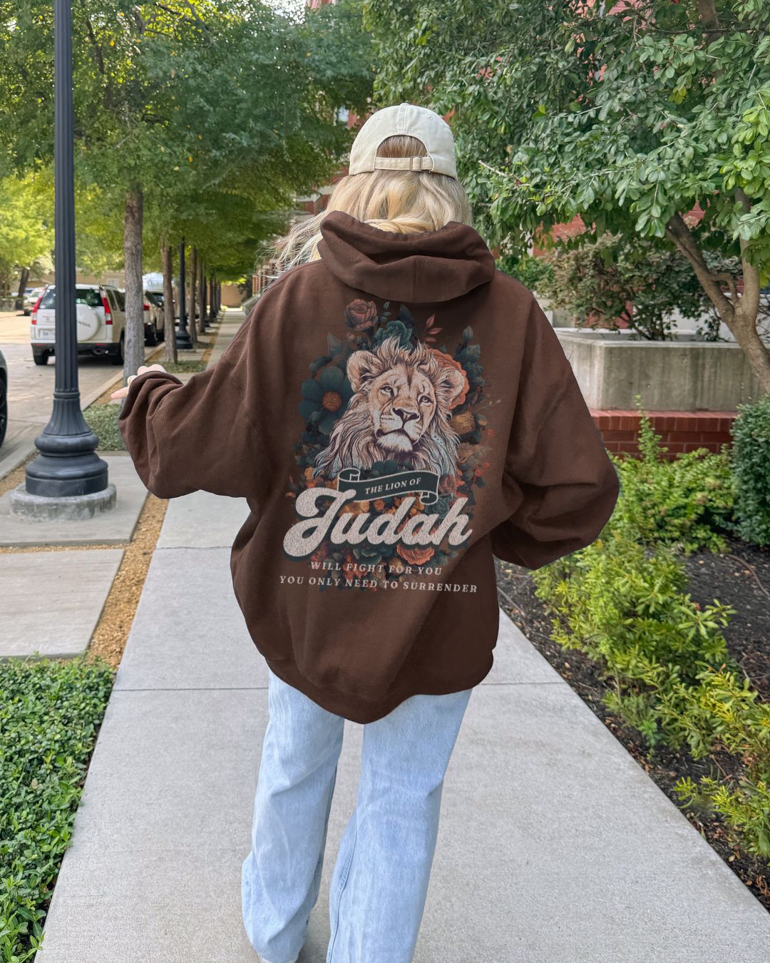 Person wearing a brown Christian hoodie with a lion graphic and 'Lion Of Judah' text, walking on a sidewalk.
