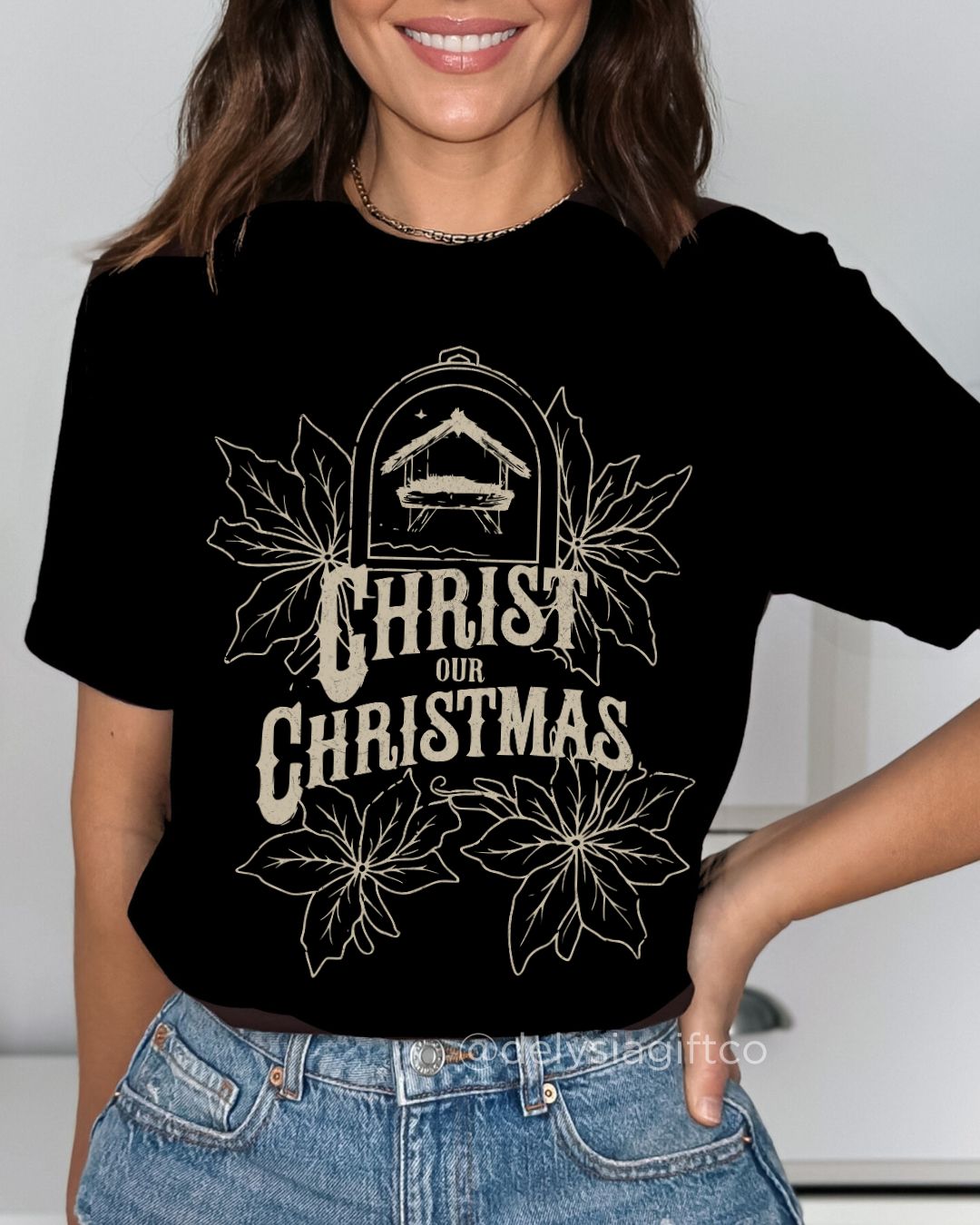 Woman wearing Christ Our Christmas Christian T-shirt with nativity design and poinsettias — faith-based apparel celebrating Jesus this holiday.