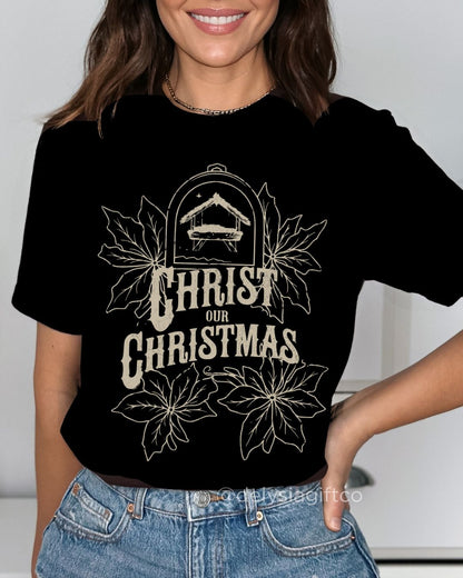 Woman wearing Christ Our Christmas Christian T-shirt with nativity design and poinsettias — faith-based apparel celebrating Jesus this holiday.