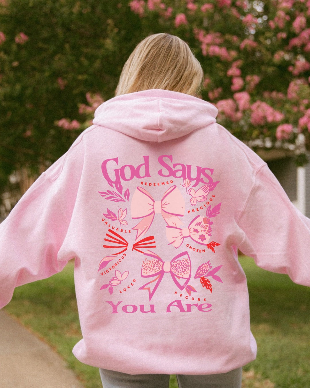 Woman wearing pink God Says You Are Christian coquette bow hoodie outdoors
