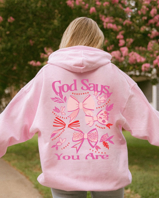 Woman wearing pink God Says You Are Christian coquette bow hoodie outdoors