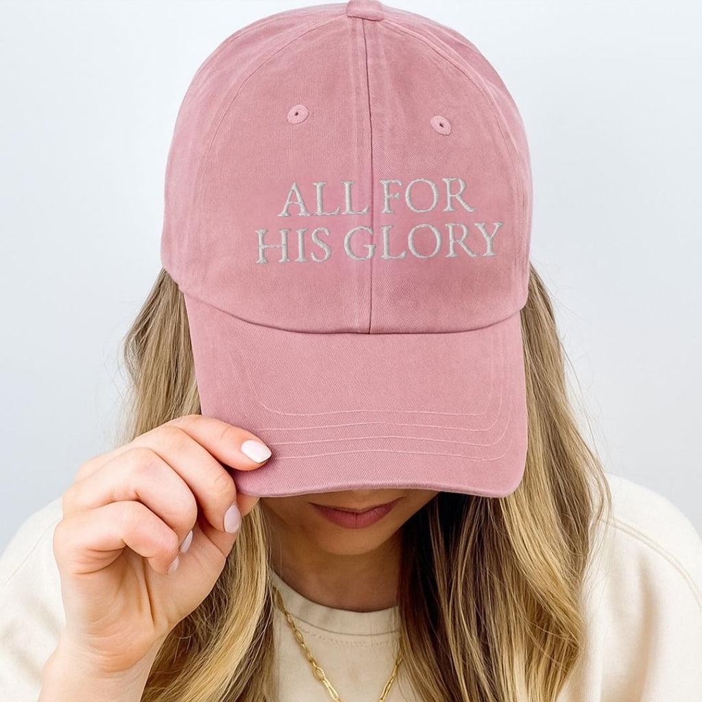 Woman wearing blush pink All for His Glory embroidered Christian baseball cap with gold necklace and neutral sweater.