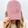 Woman wearing blush pink All for His Glory embroidered Christian baseball cap with gold necklace and neutral sweater.