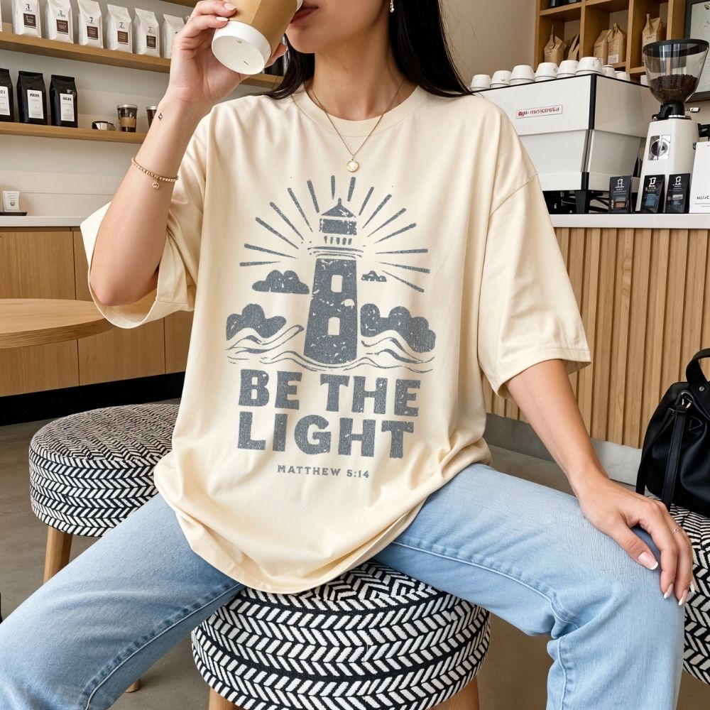 Woman wearing a Be the Light Christian t-shirt featuring a lighthouse design and Matthew 5:14 scripture