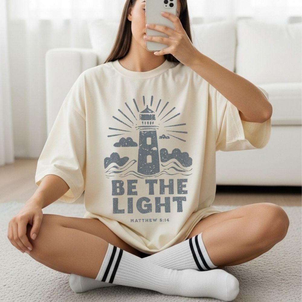 Woman wearing a Be the Light Christian t-shirt featuring a lighthouse design and Matthew 5:14 scripture