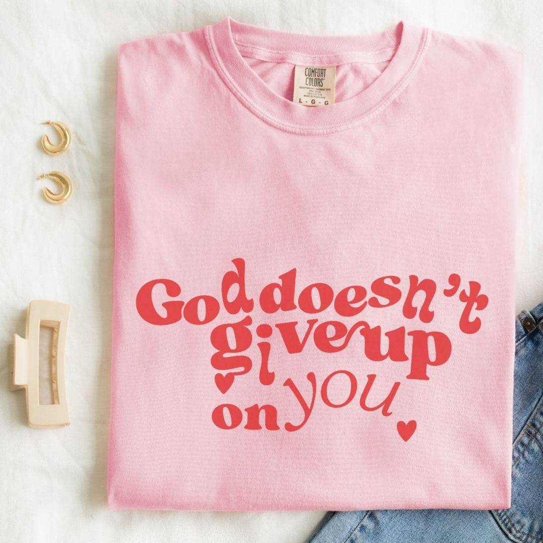 Woman wearing a pink Christian t-shirt with bold red “God Doesn’t Give Up on You” design 