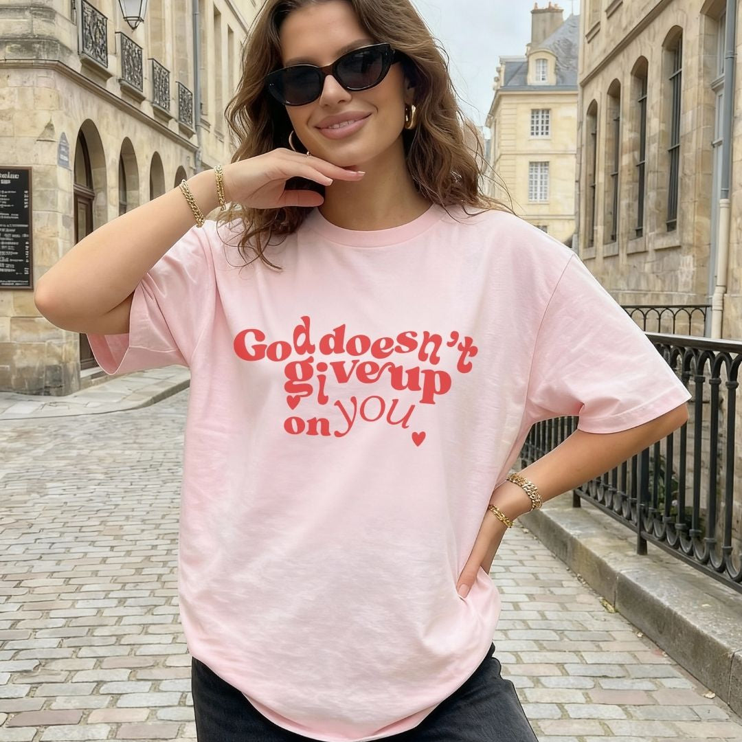 Woman wearing a pink Christian t-shirt with bold red “God Doesn’t Give Up on You” design 