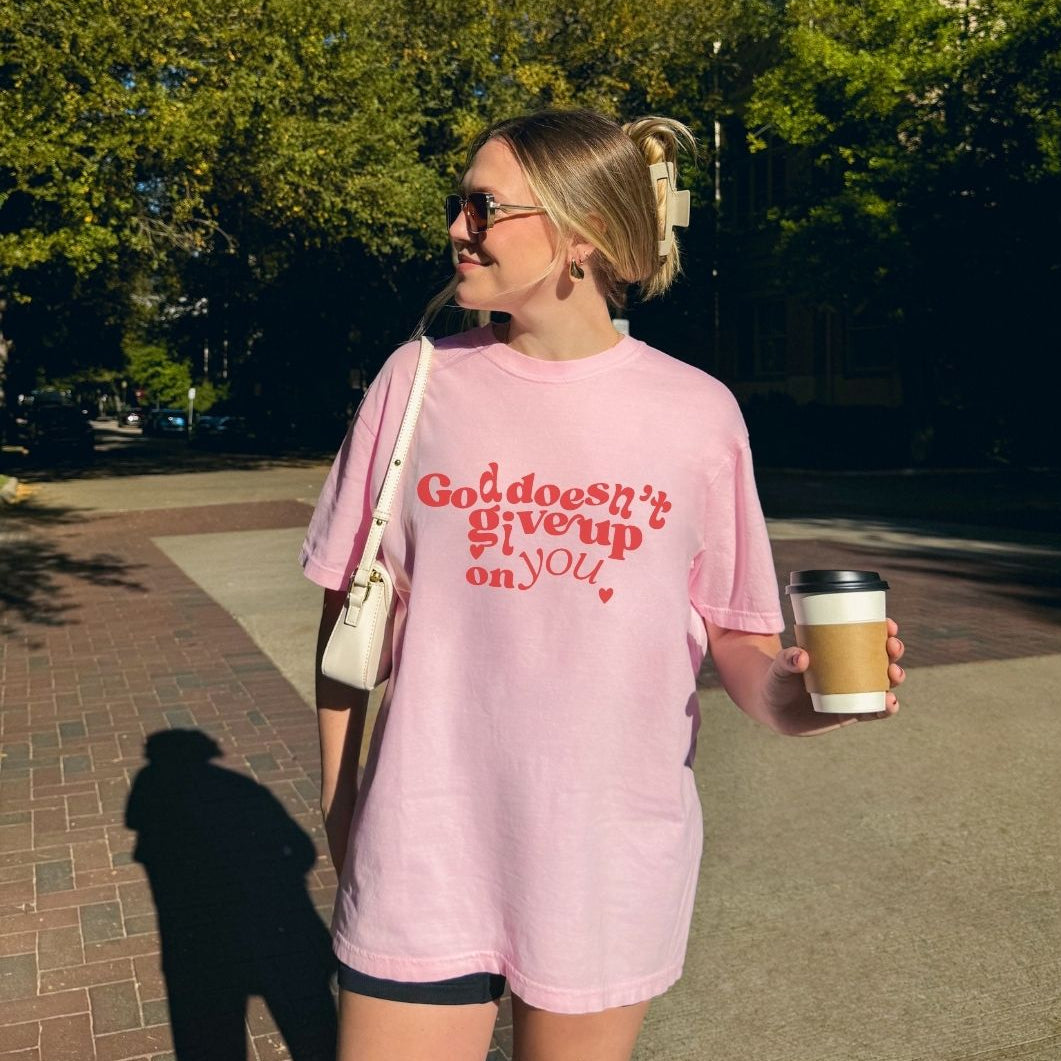 Woman wearing a pink Christian t-shirt with bold red “God Doesn’t Give Up on You” design 