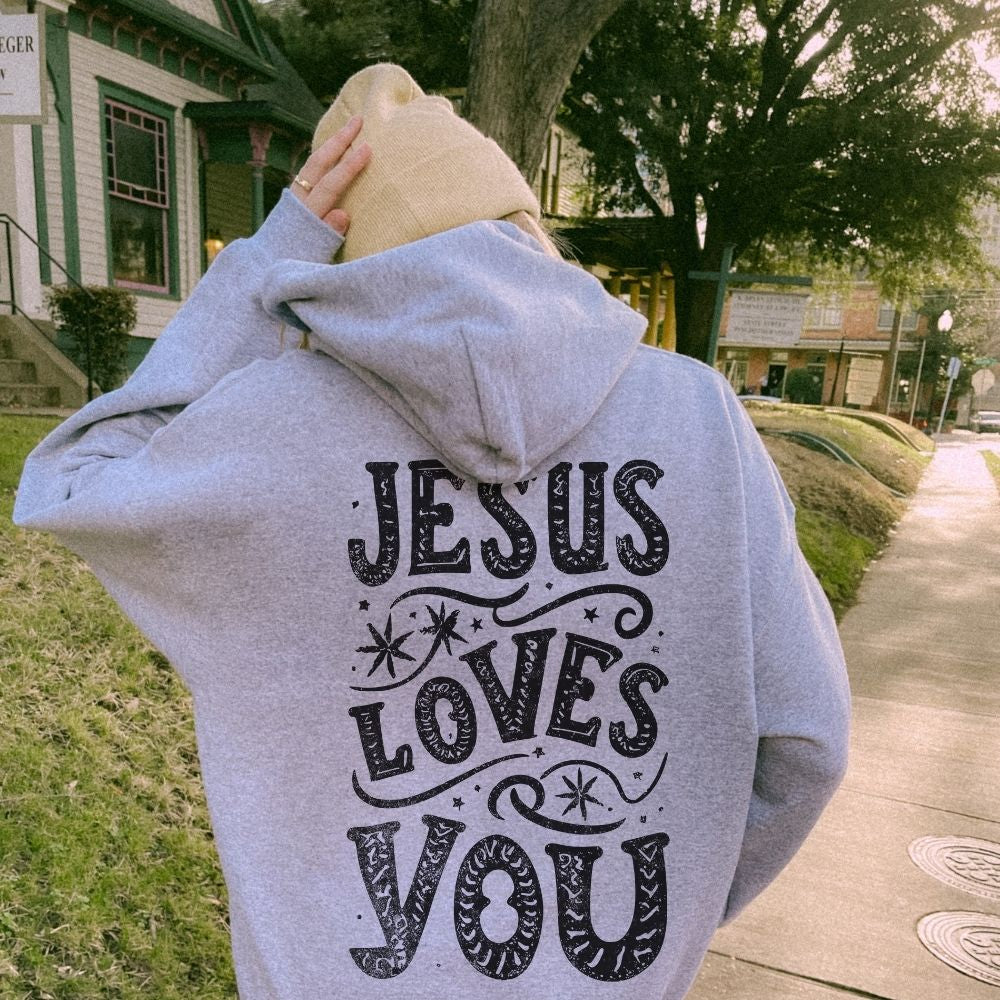 Person wearing a hoodie with 'Jesus Loves You' text outdoors.