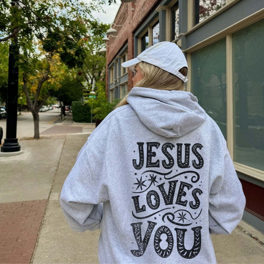 Person wearing a hoodie with 'Jesus Loves You' text on the back, walking down a street.