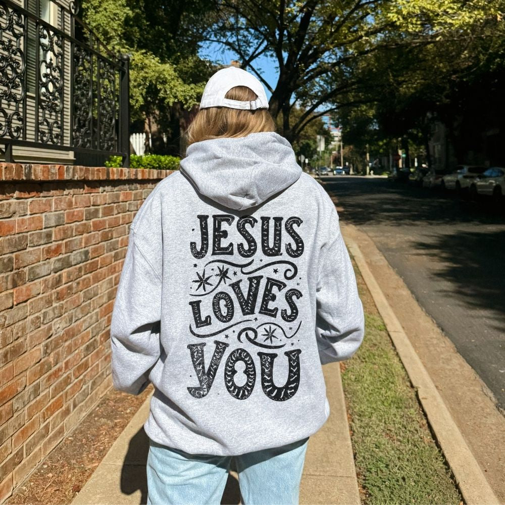 Person wearing a hoodie with 'Jesus Loves You' text on the back, walking down a street.