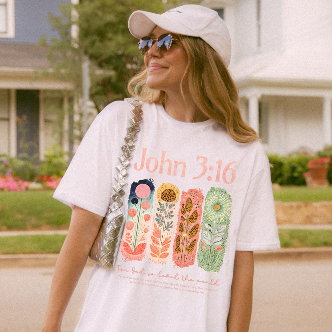 A white Christian t-shirt with a colourful hand-drawn floral bible verse design.