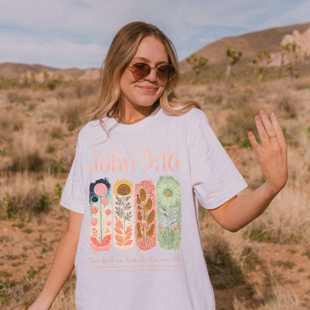 A white Christian t-shirt with a colourful hand-drawn floral bible verse design.