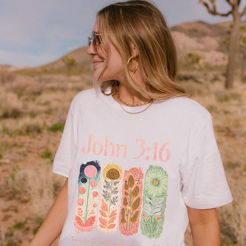 A white Christian t-shirt with a colourful hand-drawn floral bible verse design.