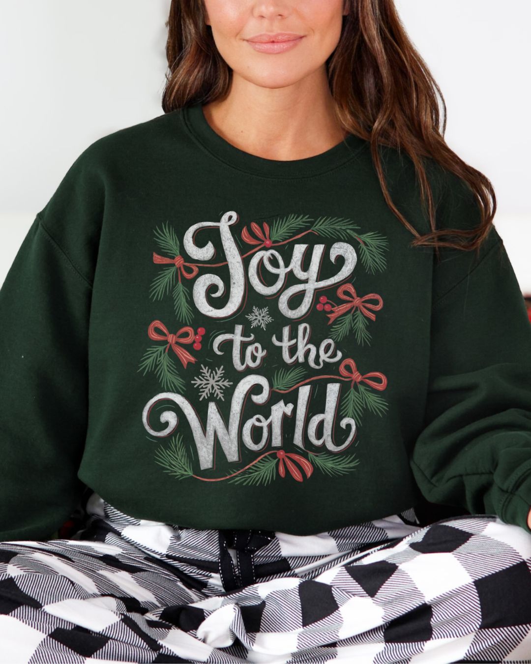 Woman wearing dark green Joy to the World Christian Christmas sweater with pine, bows, and snowflake design.