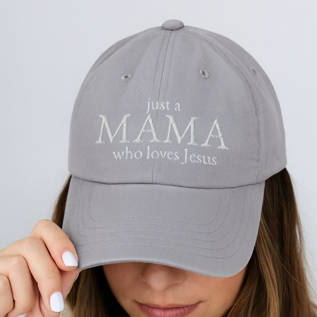 Woman wearing a Christian cap with the phrase “Just a Mama Who Loves Jesus” while holding the brim and looking down.