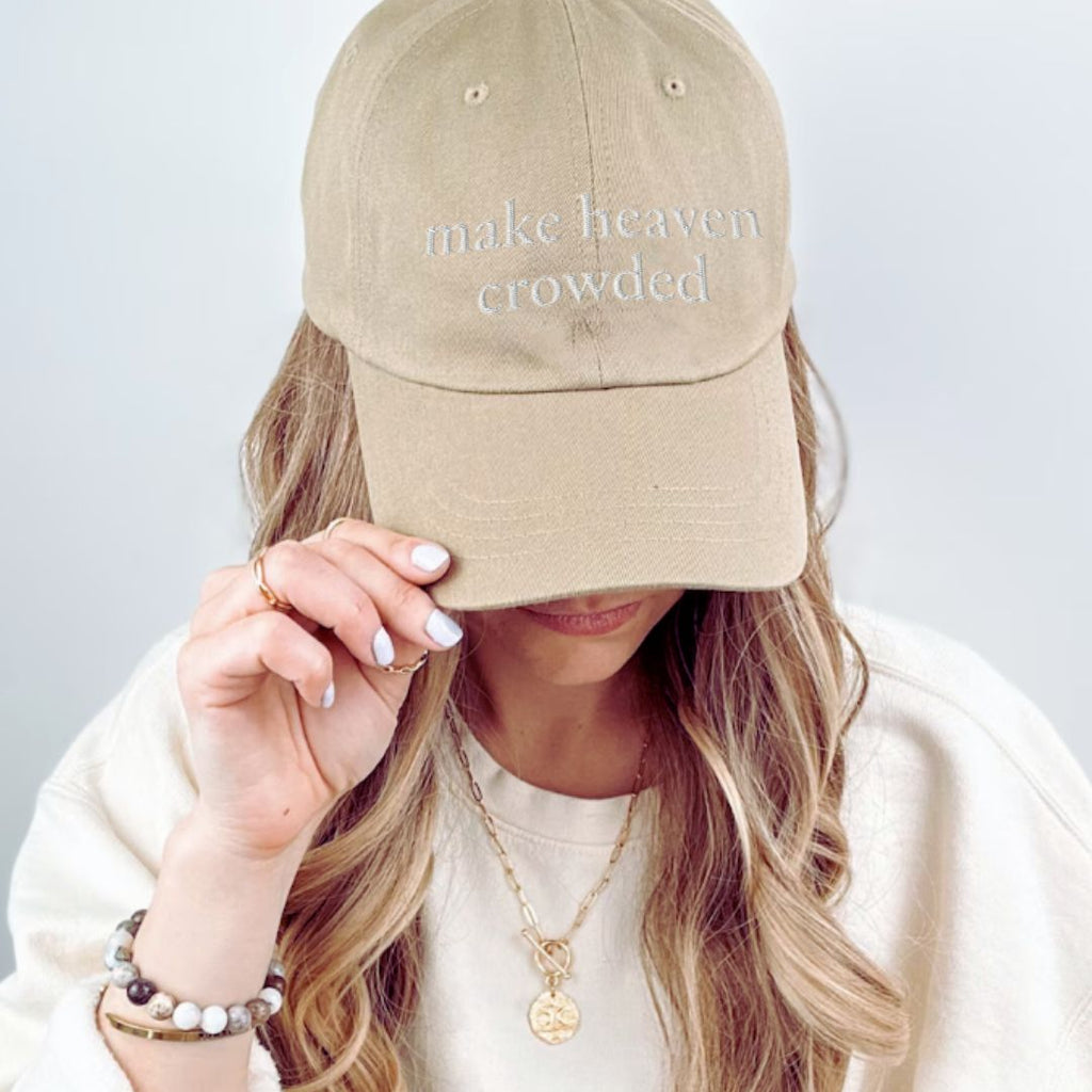 Woman wearing beige Make Heaven Crowded embroidered Christian baseball cap with neutral outfit.